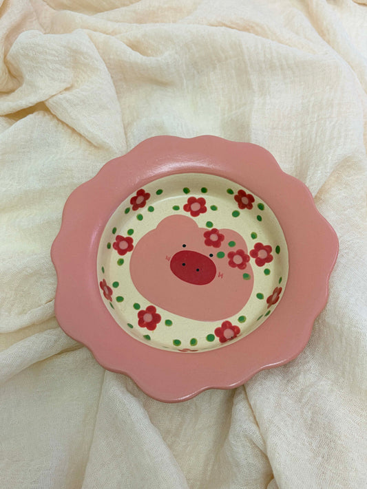 Pink children's plate with a smiley face and floral design on a white fabric background